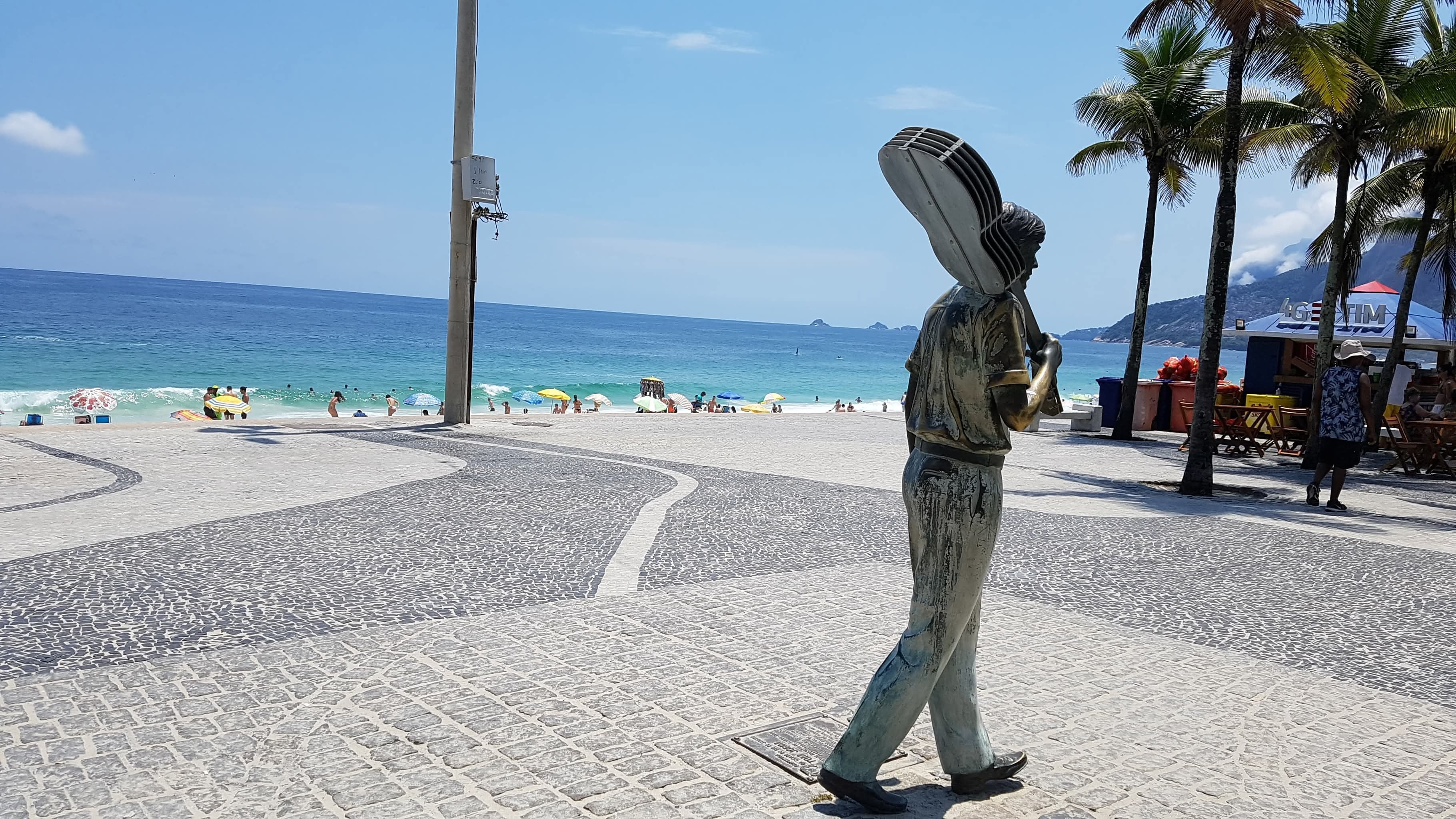 Eine Bronzestatue eines musizierenden Mannes mit Gitarre steht am sonnigen Strand