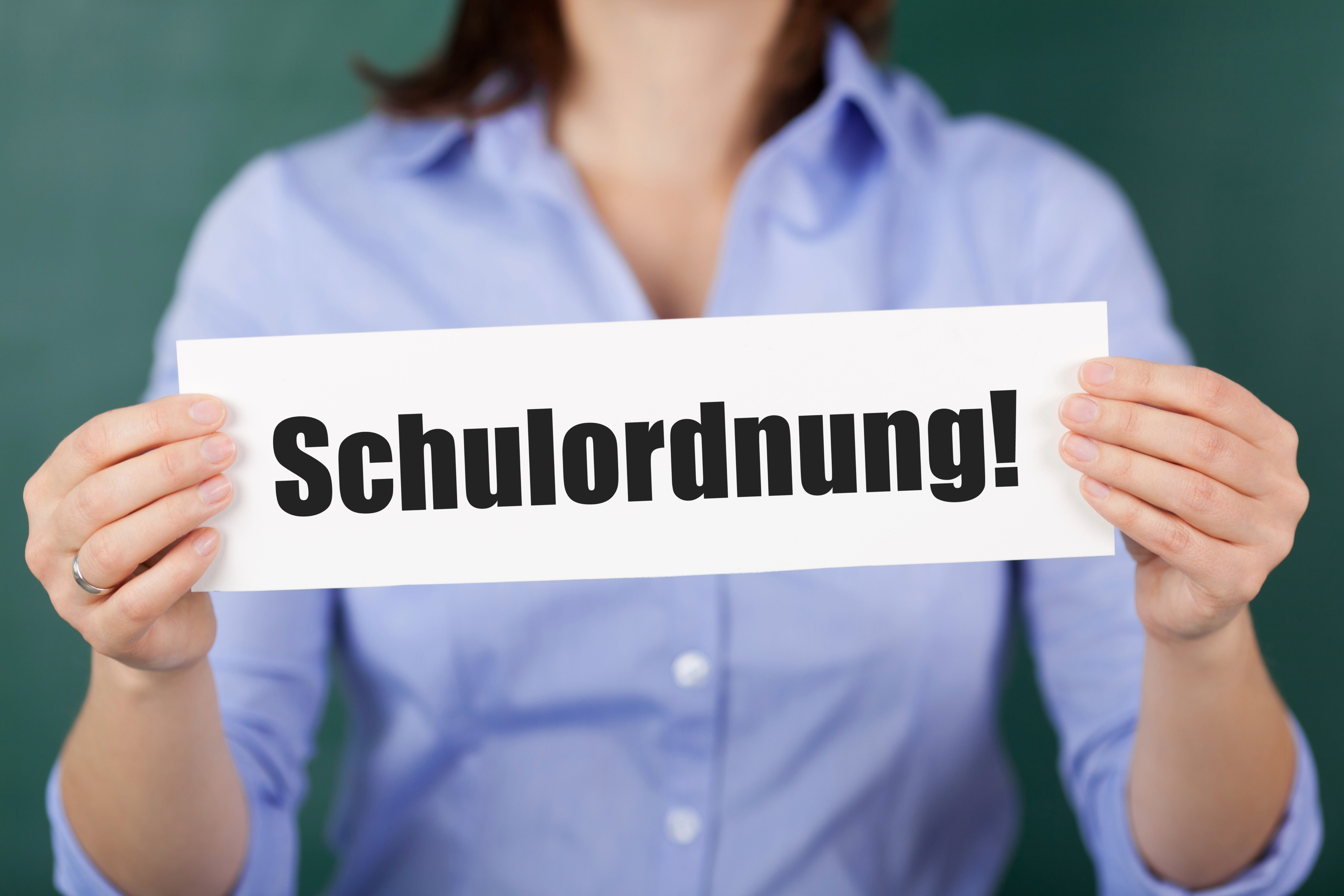 Eine Frau im blauen Hemd hält ein Schild mit schwarzer Aufschrift Schulordnung