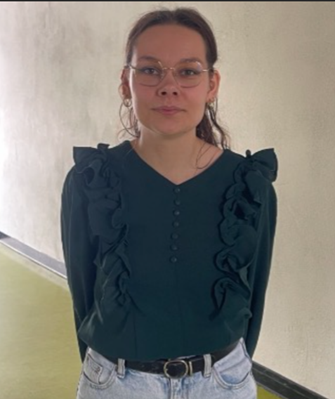 Junge Frau mit Brille, ernstem Blick, grüner Rüschenbluse und heller Jeans