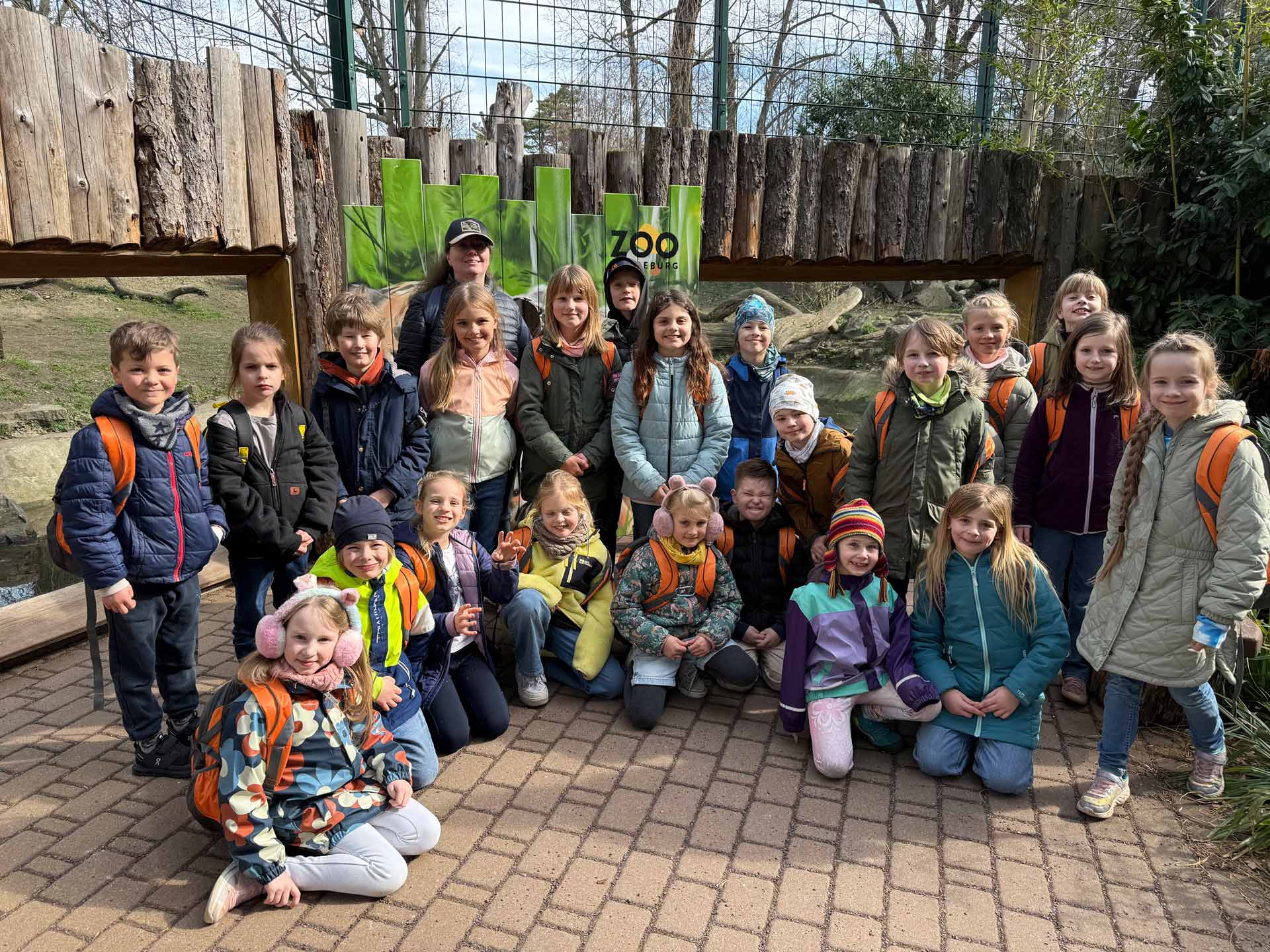 Eine Gruppe von Kindern mit bunten Jacken und fröhlichem Gesichtsausdruck im Zoo