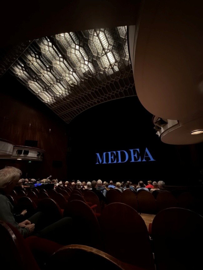 Ein halbvoller Theatersaal mit Zuschauern vor einer Bühne, auf der Medea steht