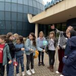 Gruppe Kinder vor blauem Glasbau, neugierig, bunt gekleidet, mit Globusmodell