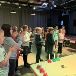Gruppe applaudierender Kinder im Musikraum vor bunten Glocken, fröhlich