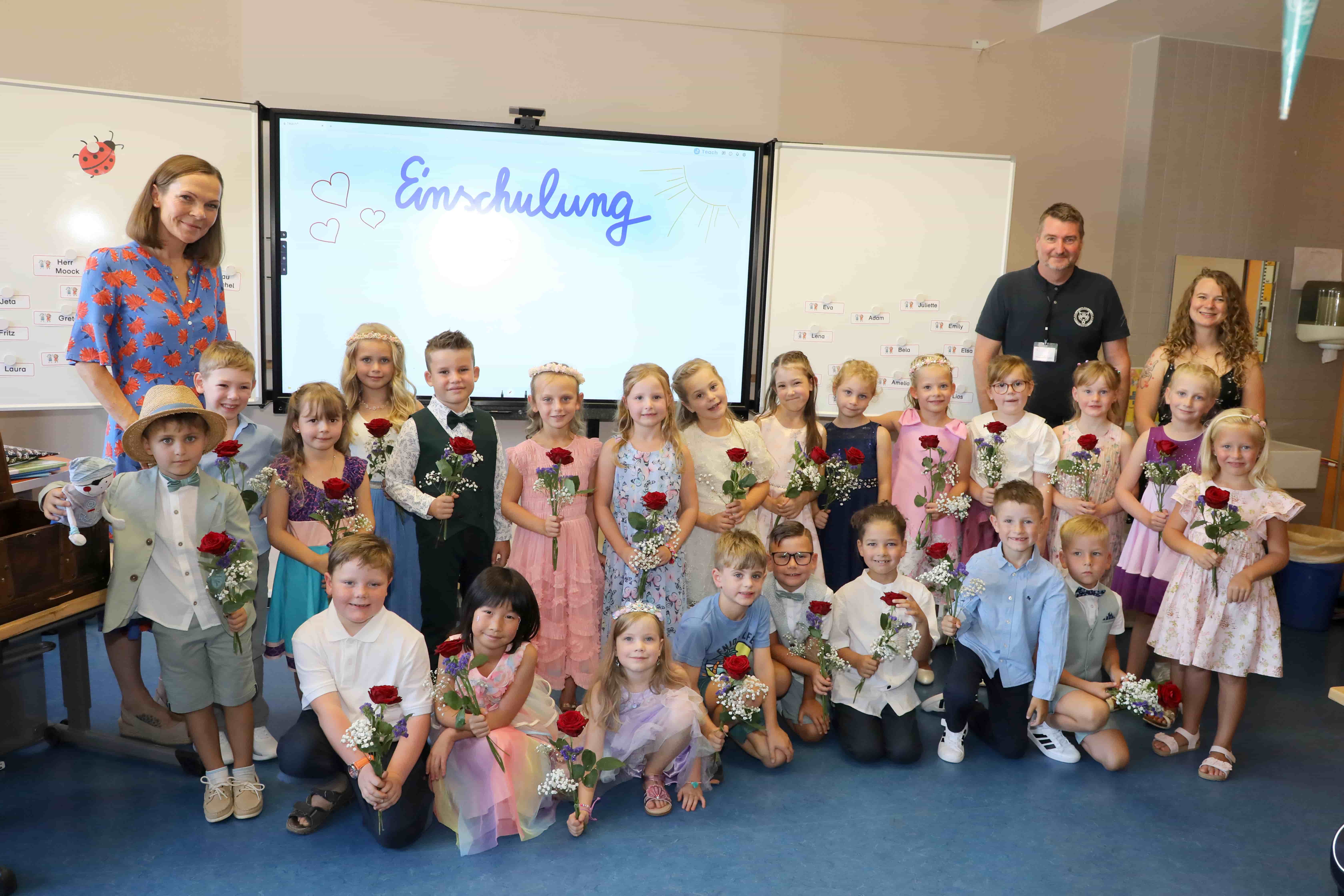 Laechelnde Kinder mit roten Rosen und drei Erwachsene bei der Einschulung