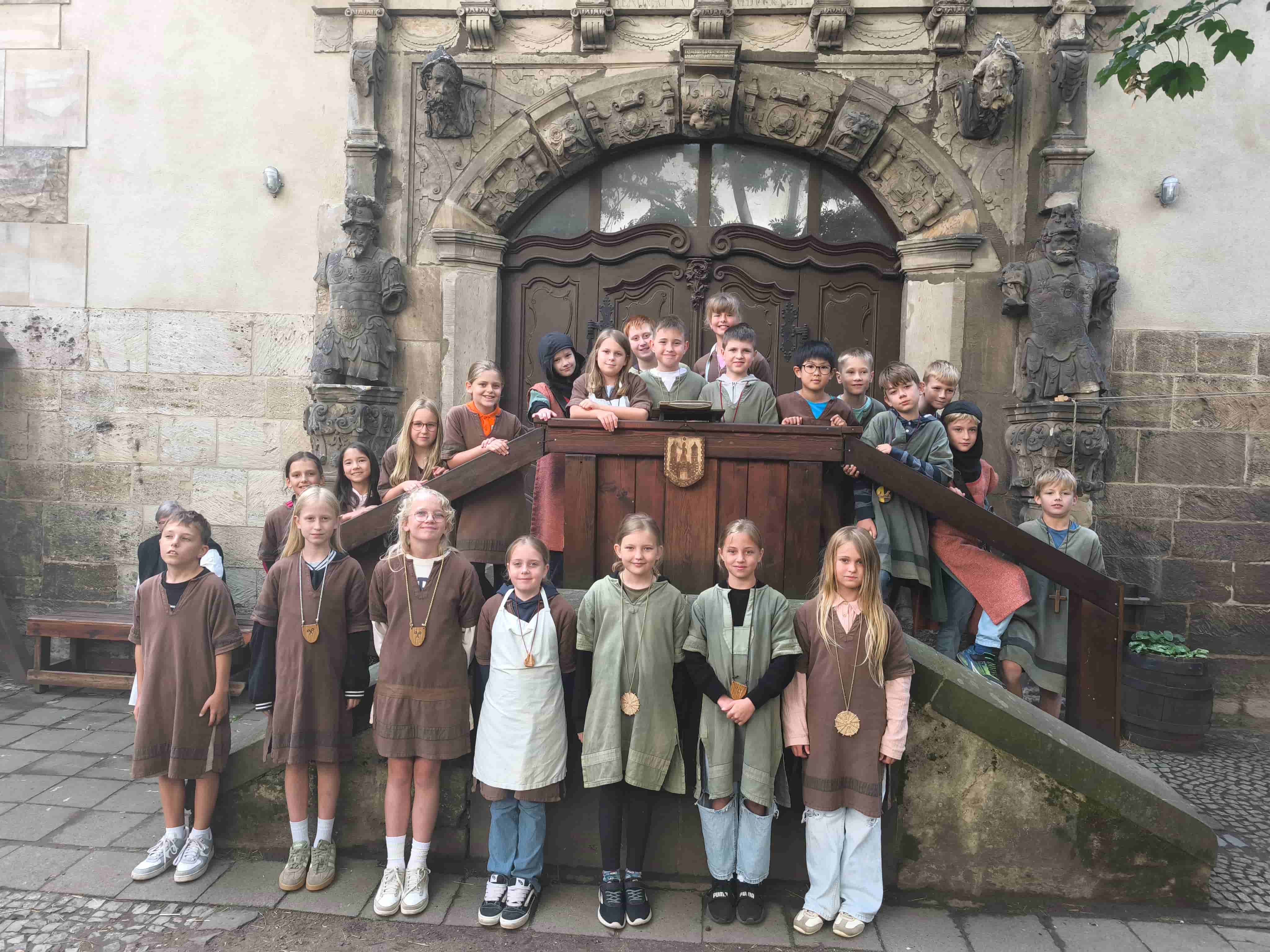 Kindergruppe in mittelalterlichen Gewaendern vor einem verzierten Steinportal