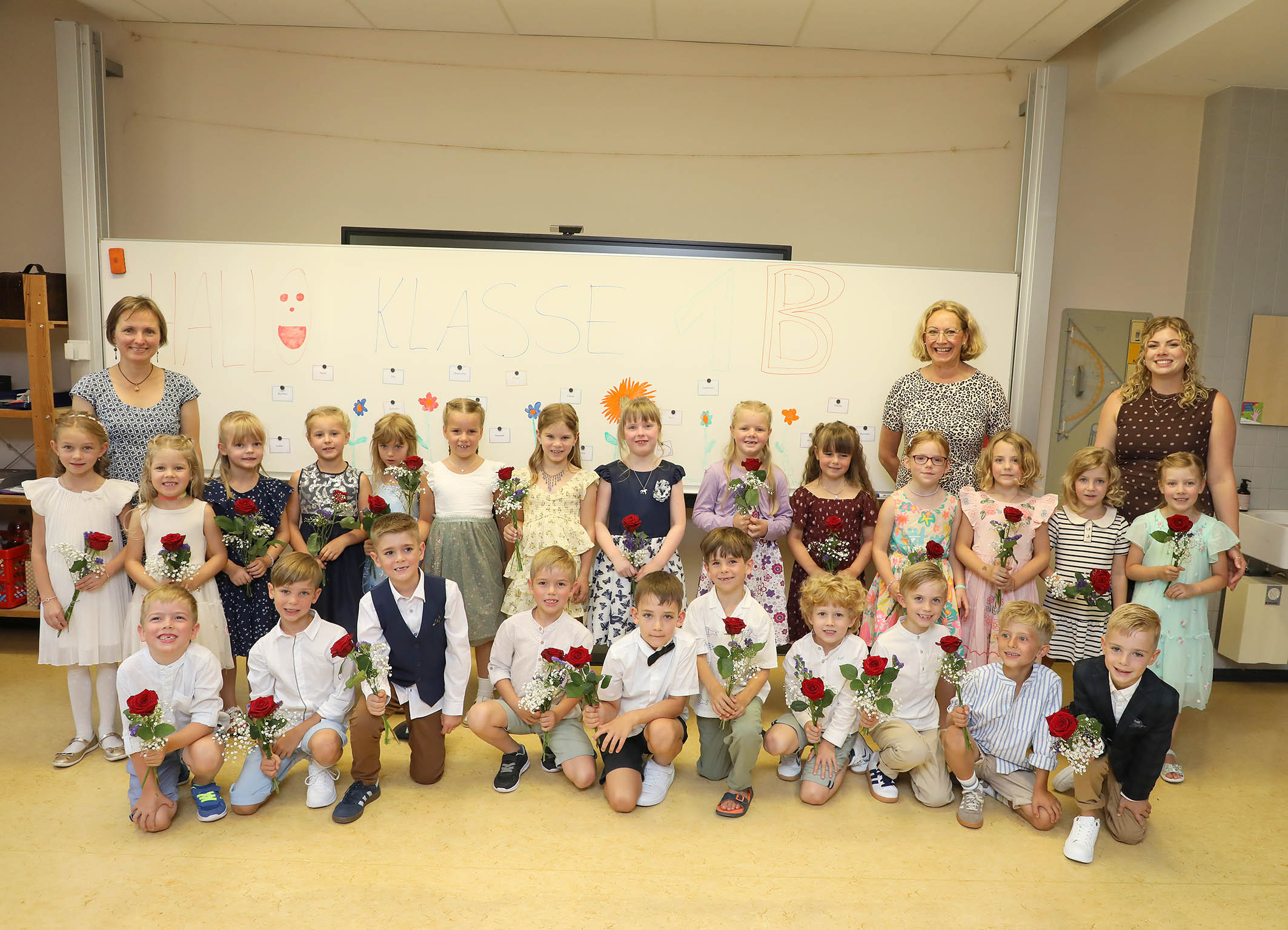 Laechelnde Erstklaesslerkinder der Klasse 1B mit roten Rosen und drei Lehrerinnen