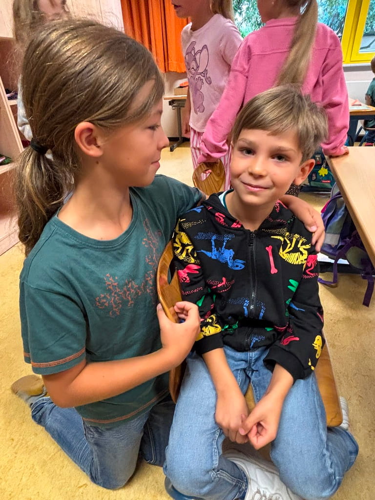 Zwei laechelnde Kinder umarmen sich freundlich in einem Klassenzimmer