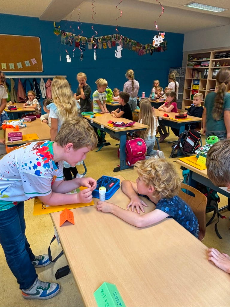 Kinder in einem bunten Klassenzimmer mit blauer Wand arbeiten an Tischen