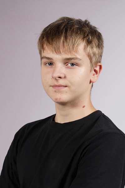 Junger Mann mit blonden Haaren und schwarzem Shirt laechelt leicht