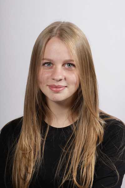 Junge Frau mit langen blonden Haaren, laechelt sanft, traegt schwarzes Oberteil