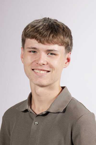 Ein laechelnder junger Mann mit braunem Haar traegt ein braunes Poloshirt