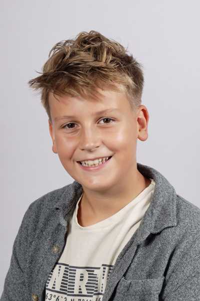 Laechelnder blonder Junge in grauer Jacke und weissem Shirt vor grauem Hintergrund