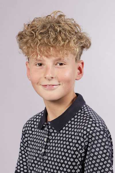 Junge mit blonden Locken laechelt in gemustertem dunklen Poloshirt