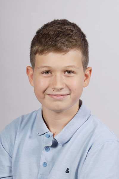 Laechelnder Junge mit kurzen braunen Haaren in hellblauem Poloshirt