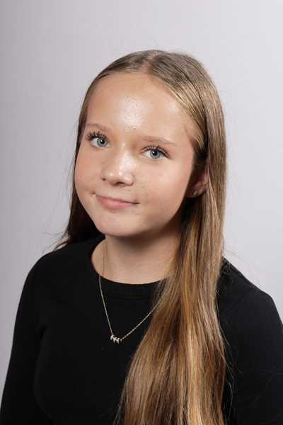 Junges Maedchen mit langen blonden Haaren laechelt leicht und traegt Schwarz