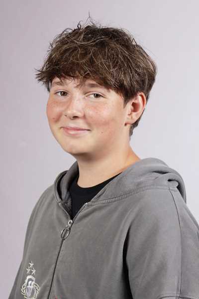 Ein laechelnder Junge mit braunen Haaren und Sommersprossen in grauer Jacke