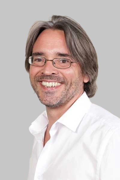Laechelnder Mann mit Brille und grauen Haaren in weissem Hemd