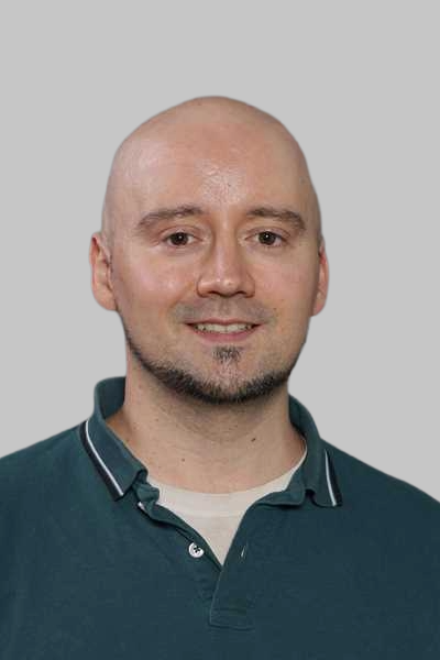 Ein laechelnder Mann mit Glatze und Kinnbart in einem dunkelgruenen Poloshirt
