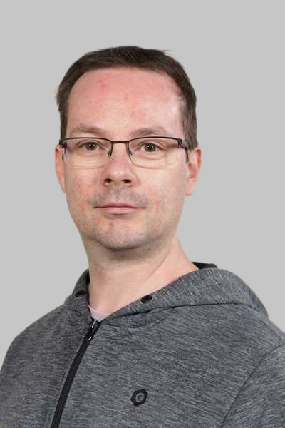 Ein Mann mit Brille und ernstem Blick traegt eine graue Kapuzenjacke