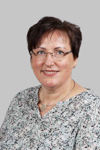 Laechelnde Frau mit Brille und gemusterter Bluse vor grauem Hintergrund