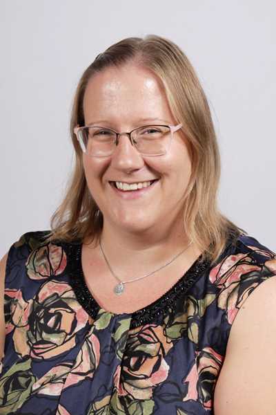 Laechelnde Frau mit Brille und blonden Haaren in geblumter Bluse