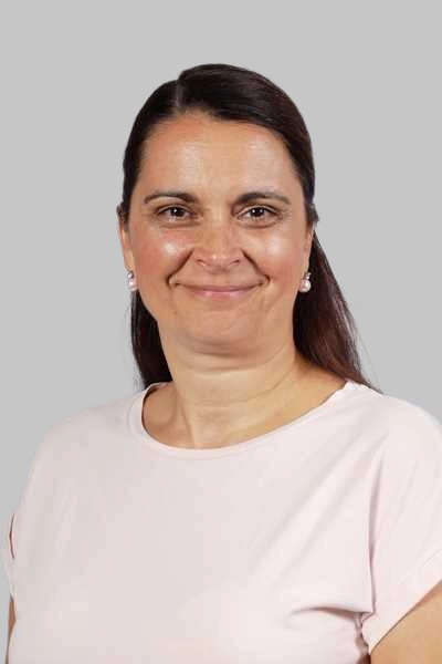 Laechelnde Frau mit dunklen Haaren in rosa Shirt vor grauem Hintergrund