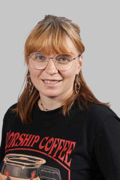Laechelnde Frau mit rotbraunem Haar Brille und schwarzem Shirt mit rotem Aufdruck
