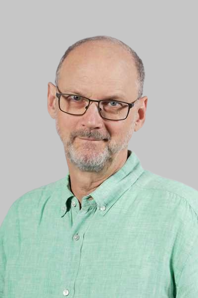 Ein Mann mit Brille und grauem Bart traegt ein gruenes Hemd