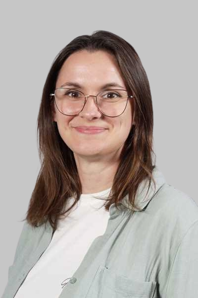 Laechelnde Frau mit Brille braunen Haaren und gruenem Hemd vor grauem Grund