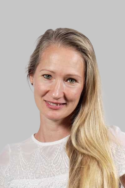 Laechelnde blonde Frau in weisser Spitzenbluse vor grauem Hintergrund