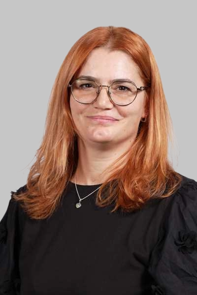 Laechelnde Frau mit rotem Haar und Brille traegt schwarze Bluse