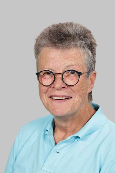 Laechelnde Frau mit kurzen grauen Haaren und Brille im hellblauen Poloshirt