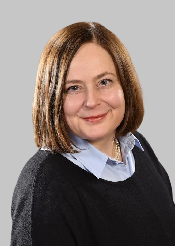 Laechelnde Frau mit braunem Haar in dunklem Pullover und blauer Bluse