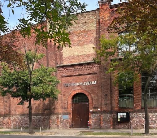 Rotes Backsteingebaeude des Technikmuseums mit Bogeneingang und Baeumen davor