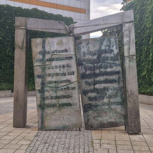 Ein graues Bronzedenkmal mit zwei beschrifteten Tafeln vor gruener Wand