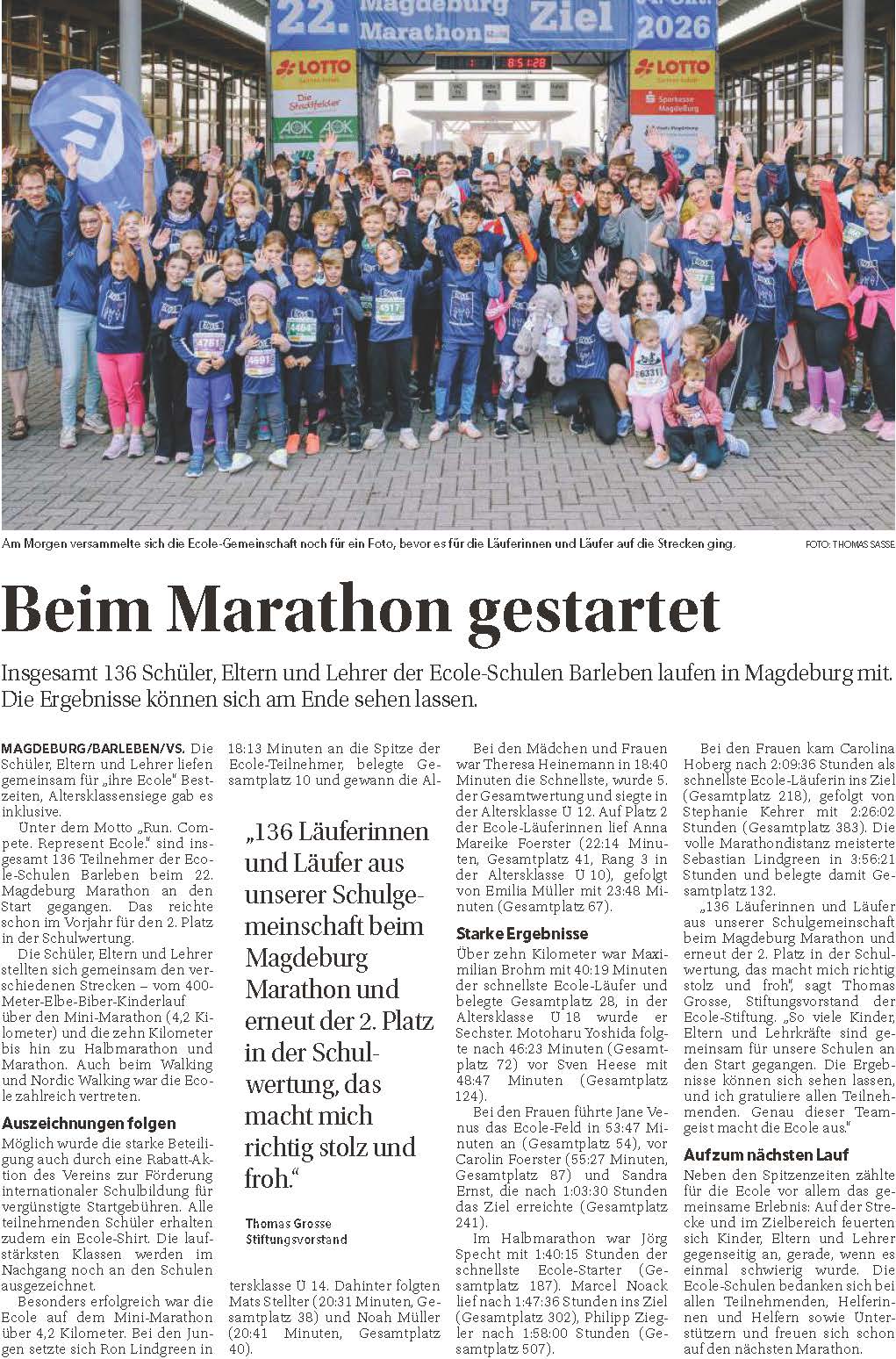 Grosse jubelnde Laufergruppe in blauen Shirts vor dem Marathon Zielbogen
